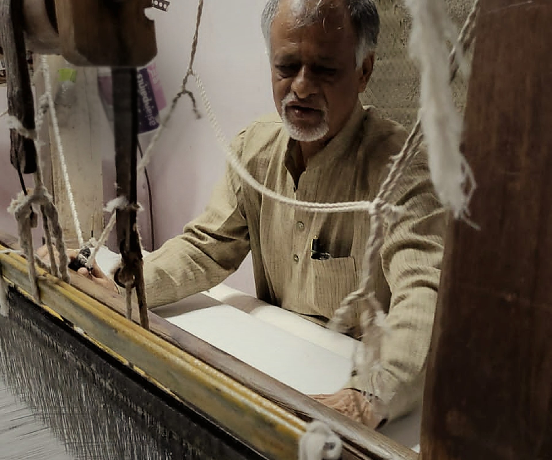 A weaver at the pit loom, hands at the tope teni pallu, low warm light